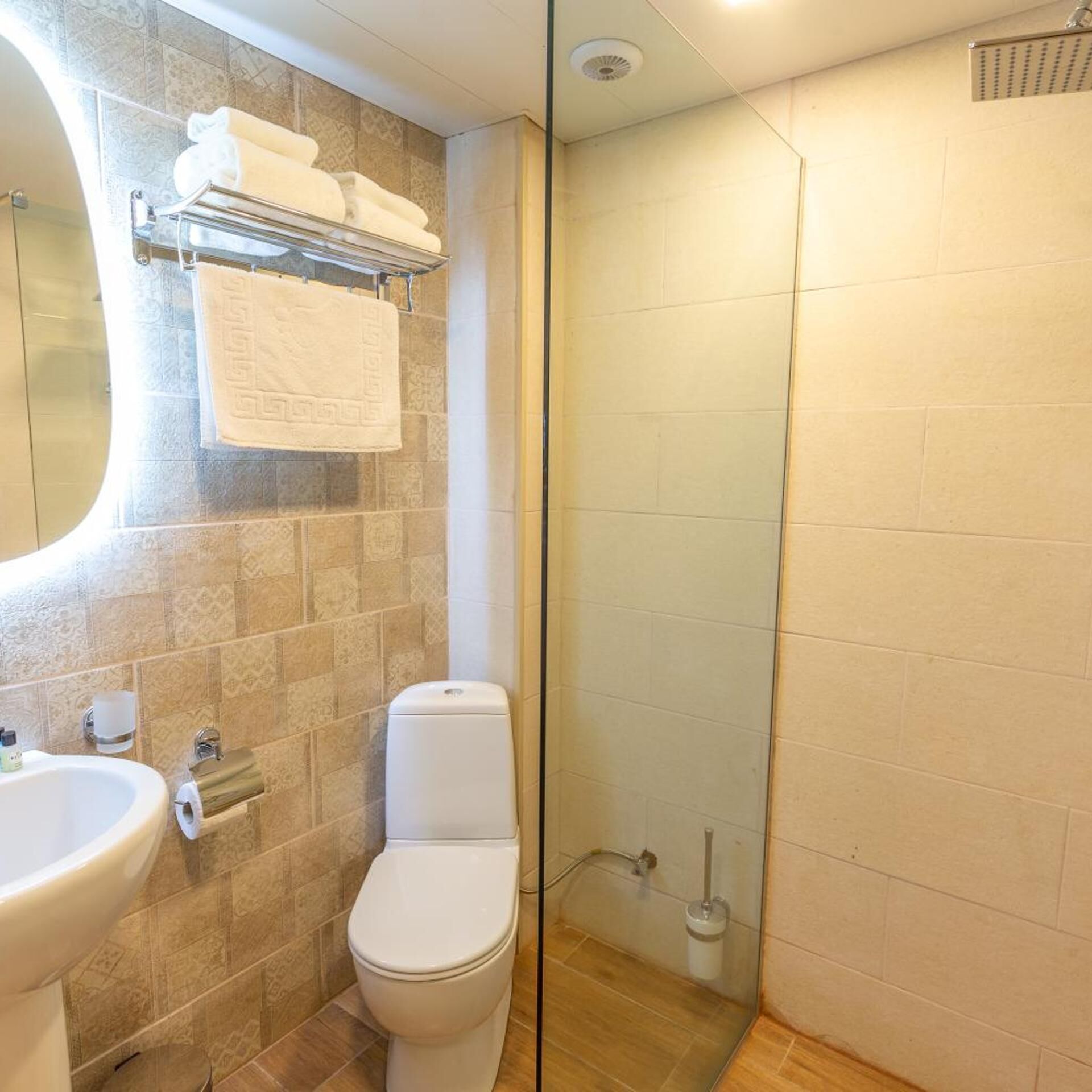 Baño con inodoro, lavamanos y cabina de ducha con paredes de vidrio.