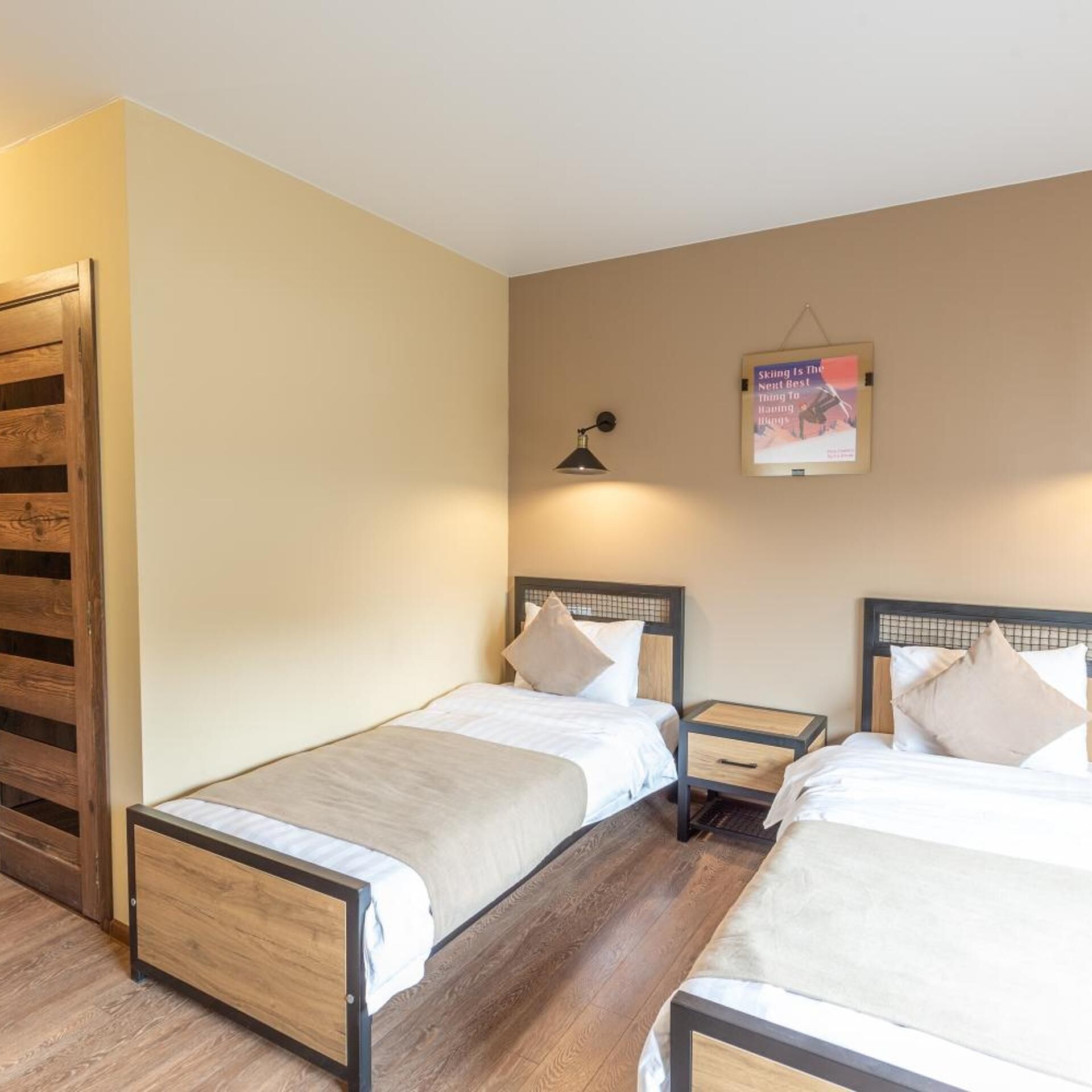 Habitación de hotel con dos camas individuales, un armario de madera, una mesita de noche con lámpara y un cartel en la pared.