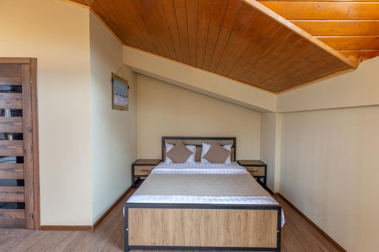 A bedroom with a wooden ceiling, a bed with a headboard, two bedside tables, and a wall-mounted picture.