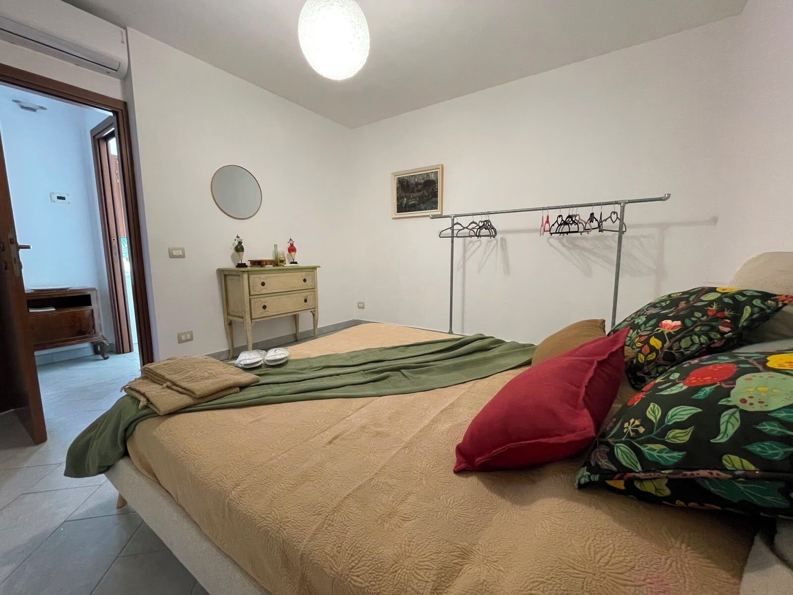 Une chambre à coucher avec un lit, une commode, un miroir et un portant à vêtements.