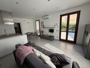A modern living space with a sofa, a dining area, a kitchen, and a sliding glass door leading to an outdoor area.