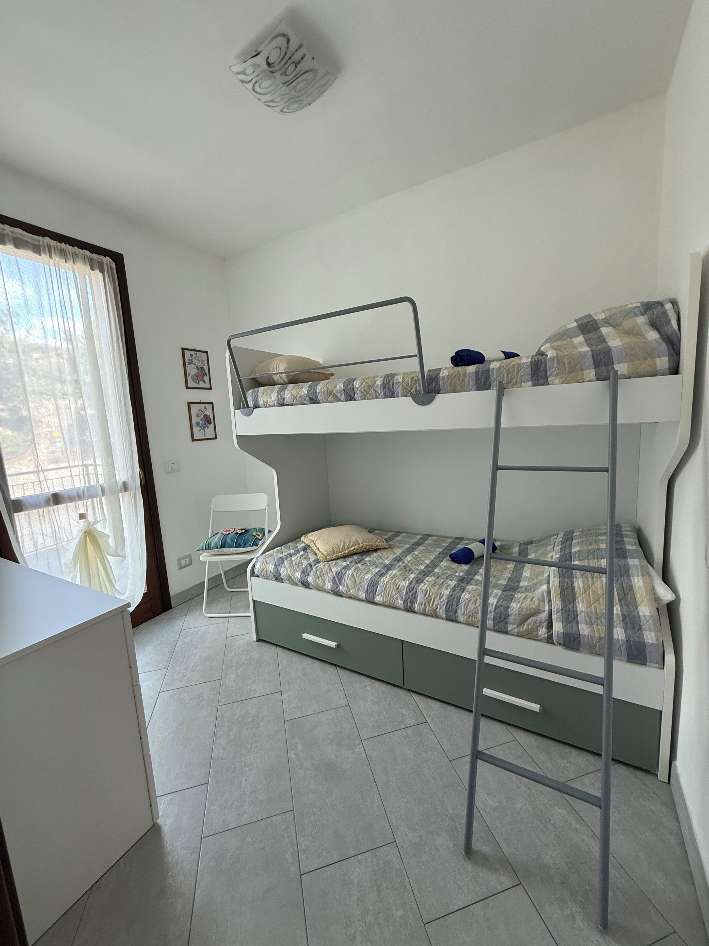 Una stanza con un letto a castello, una scrivania, una sedia e una finestra con tende.