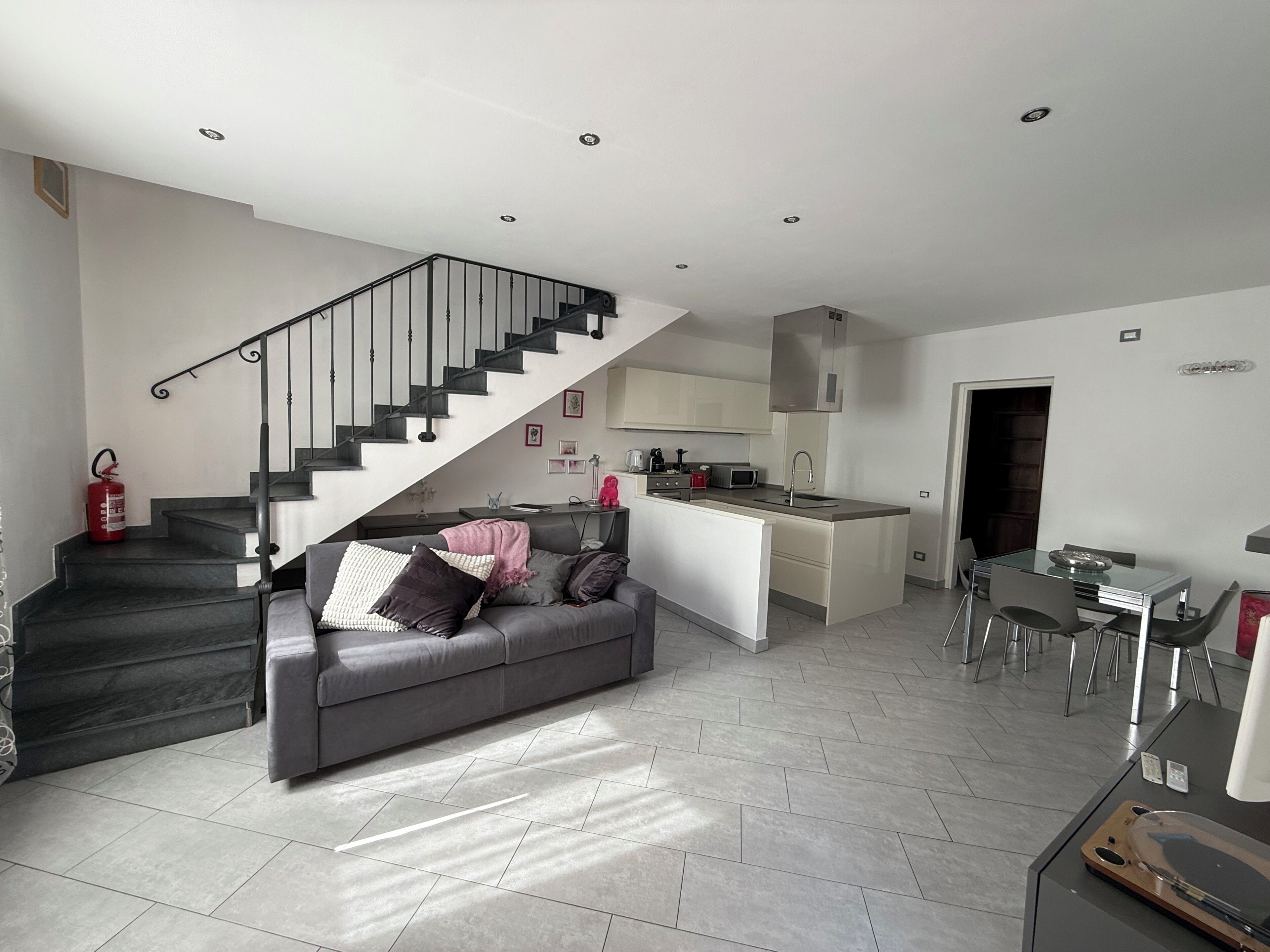 A modern living space with a staircase, a sofa, a kitchen island, and a dining area.
