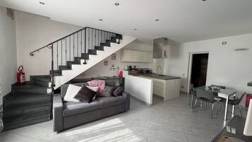 A modern living space with a staircase, a sofa, a kitchen island, and a dining area.