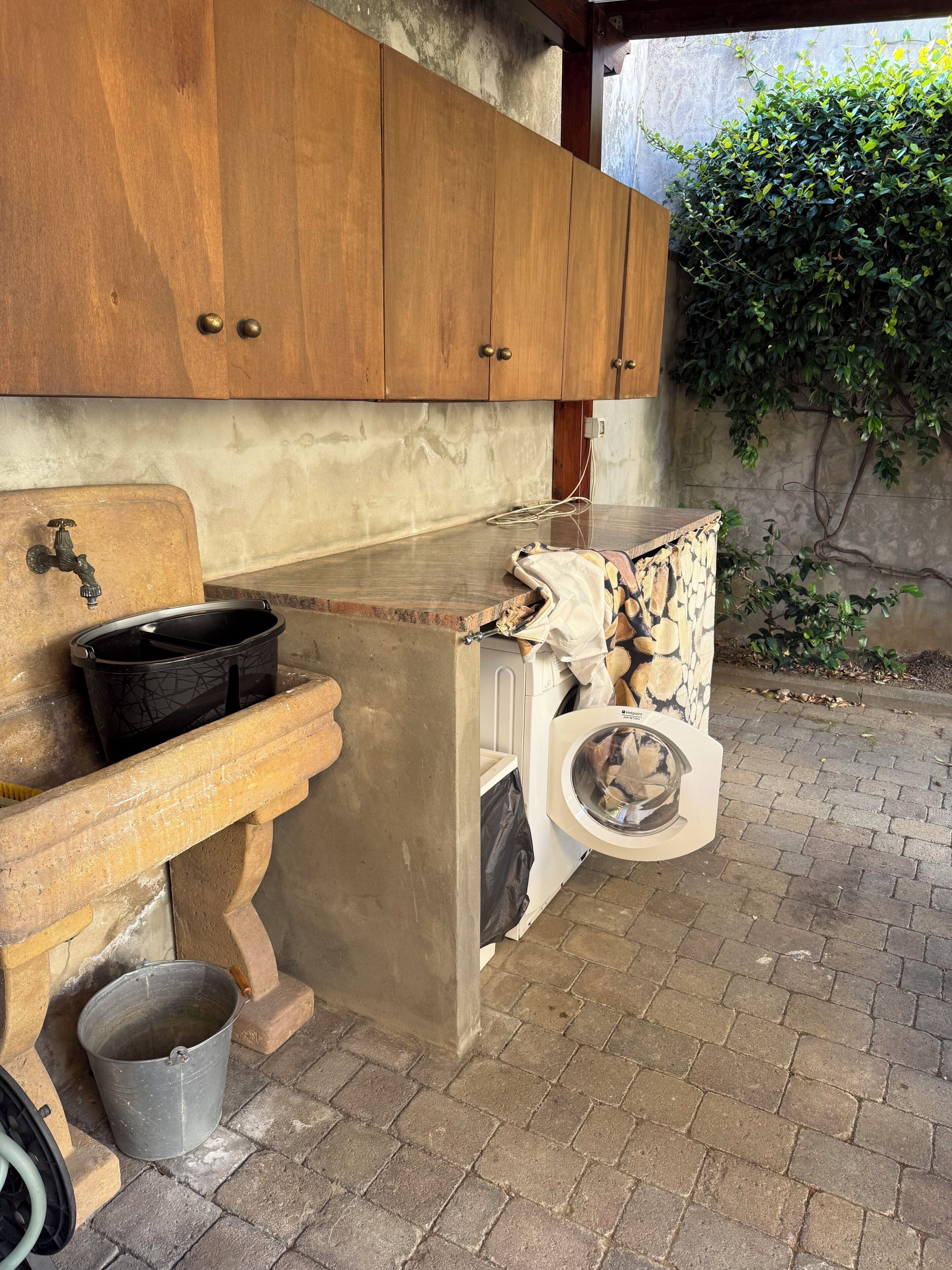 A rustic outdoor kitchen with wooden cabinets, a sink, and a washing machine.