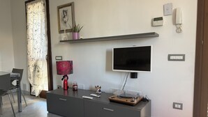 Een moderne woonkamer met een flatscreen televisie, een console tafel, een rode lamp en een 'BENVENUTI' welkomstmat.
