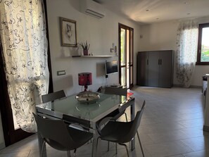 A modern kitchen with a glass dining table, two chairs, a TV, and a cabinet.