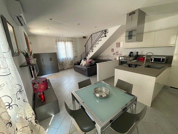 A modern kitchen with a built-in microwave, a dining area with a glass table, and a staircase leading to a loft bedroom.