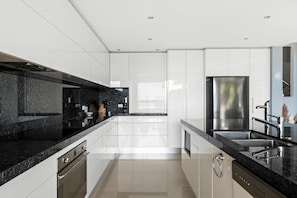 Uma cozinha moderna com armários brancos, bancadas pretas, eletrodomésticos de aço inoxidável e piso revestido.