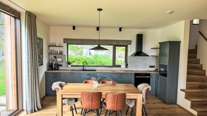 Uma cozinha moderna com área de refeições, piso de madeira e vista para o verde lá fora.