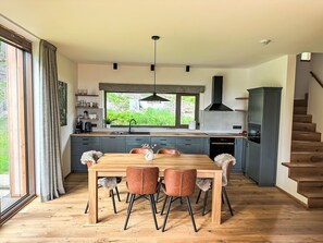 A modern kitchen with a dining area, wooden flooring, and a view of greenery outside. - Rebelka by Interhome (Horni Misecky)