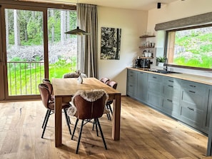 A modern kitchen with a large island, wooden flooring, and a dining area with a table and chairs. - Rebelka by Interhome (Horni Misecky)