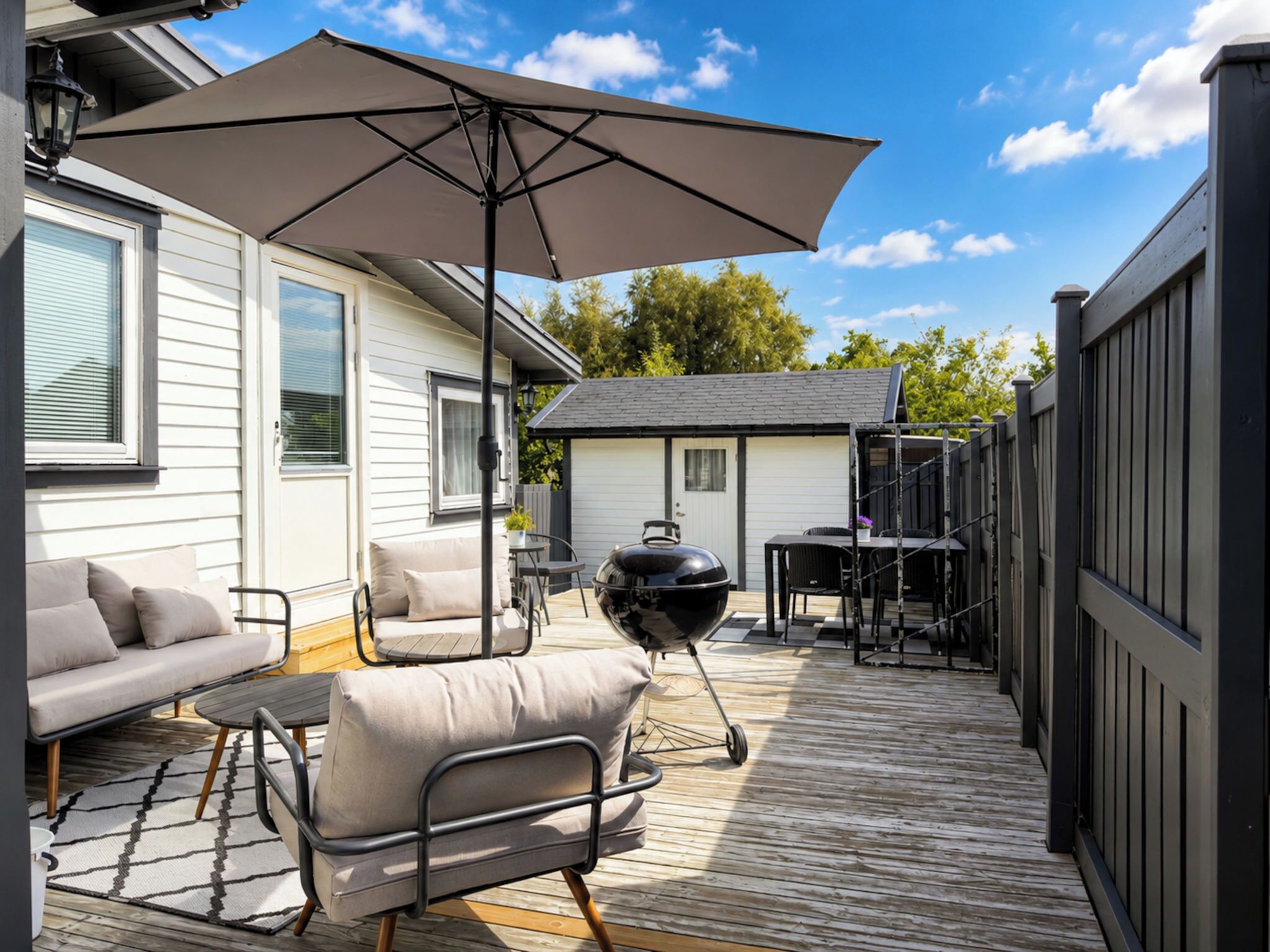 Une terrasse avec des meubles d’extérieur, un barbecue et un espace abrité avec un parasol.
