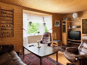 Ein gemütliches Wohnzimmer mit einer Ledersofa, einem braunen Ledersessel, einem Holztisch, einem Fernseher und einem Regal mit verschiedenen Gegenständen.