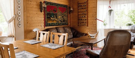 A cozy wooden interior with a dining table, chairs, a sofa, and a large decorative painting.