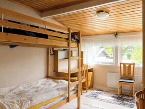 Ein Schlafraum mit Etagenbetten, einem Schreibtisch und Stuhl, einem Heizkörper und einem Fenster mit Blick auf Grünflächen.