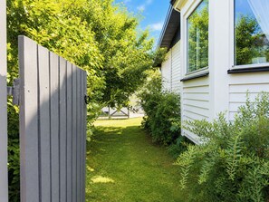 Ein Wohnhaus mit umzäunter Garten, Rasenfläche und weiß verputzten Fassaden.