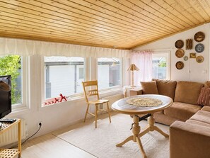 Ein gemütliches Wohnzimmer mit Holzbalkendecke, einem runden Tisch mit Spitzeentdecke, einem beigen Sofa und einem Holzstuhl.
