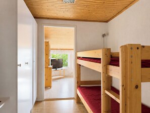 Une chambre avec des lits superposés, une télévision et une porte donnant sur une autre pièce.