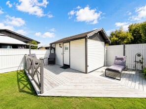Eine Terrasse mit Grill, einer kleinen Gartenhütte und einer Liege.