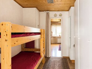 Um quarto com uma cama beliche, teto de madeira, porta que dá para outro quarto e um tapete estampado no chão.