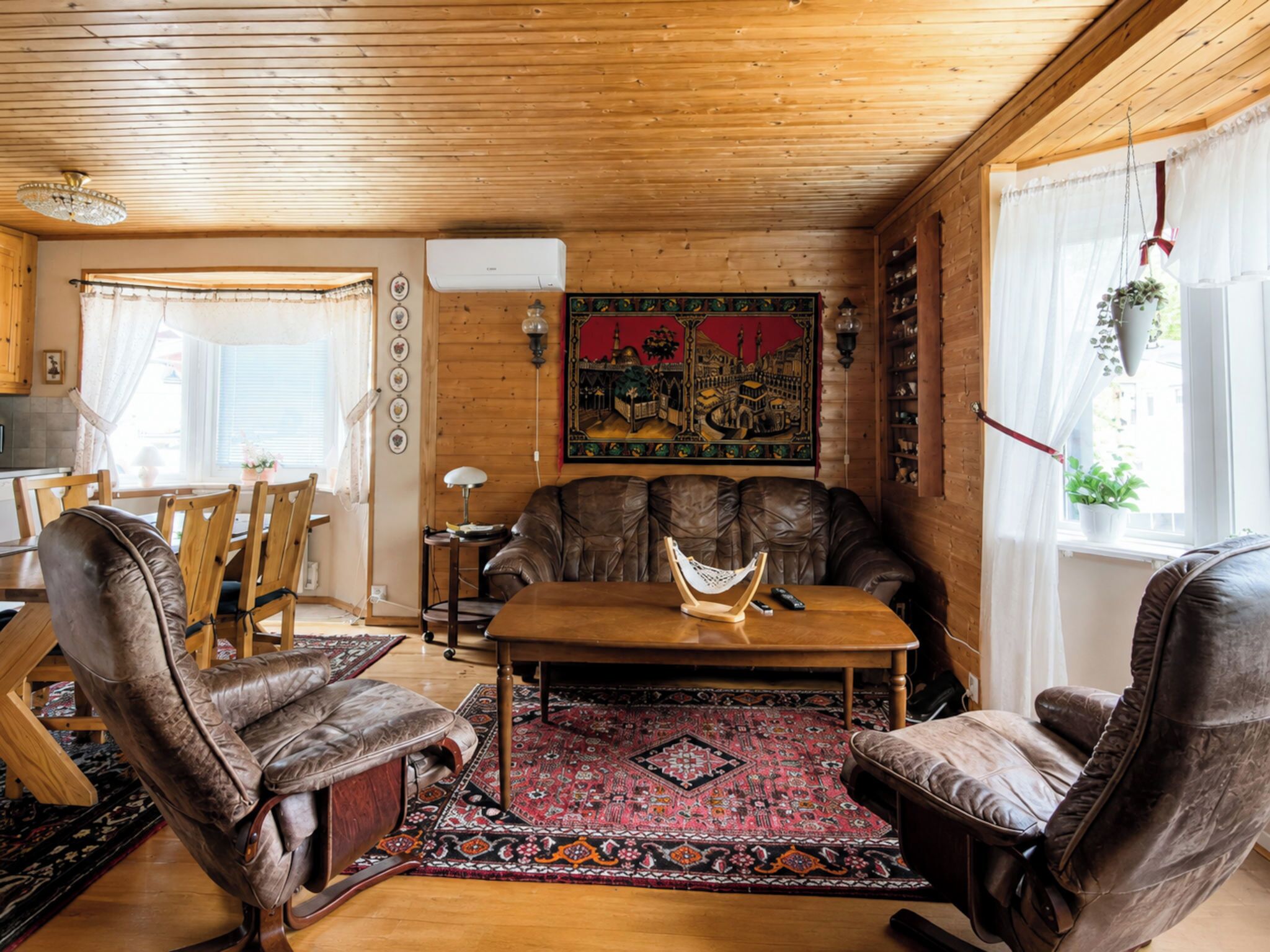 En ombonad träinredning med en soffa i läder, ett matbord och en mönstrad matta.