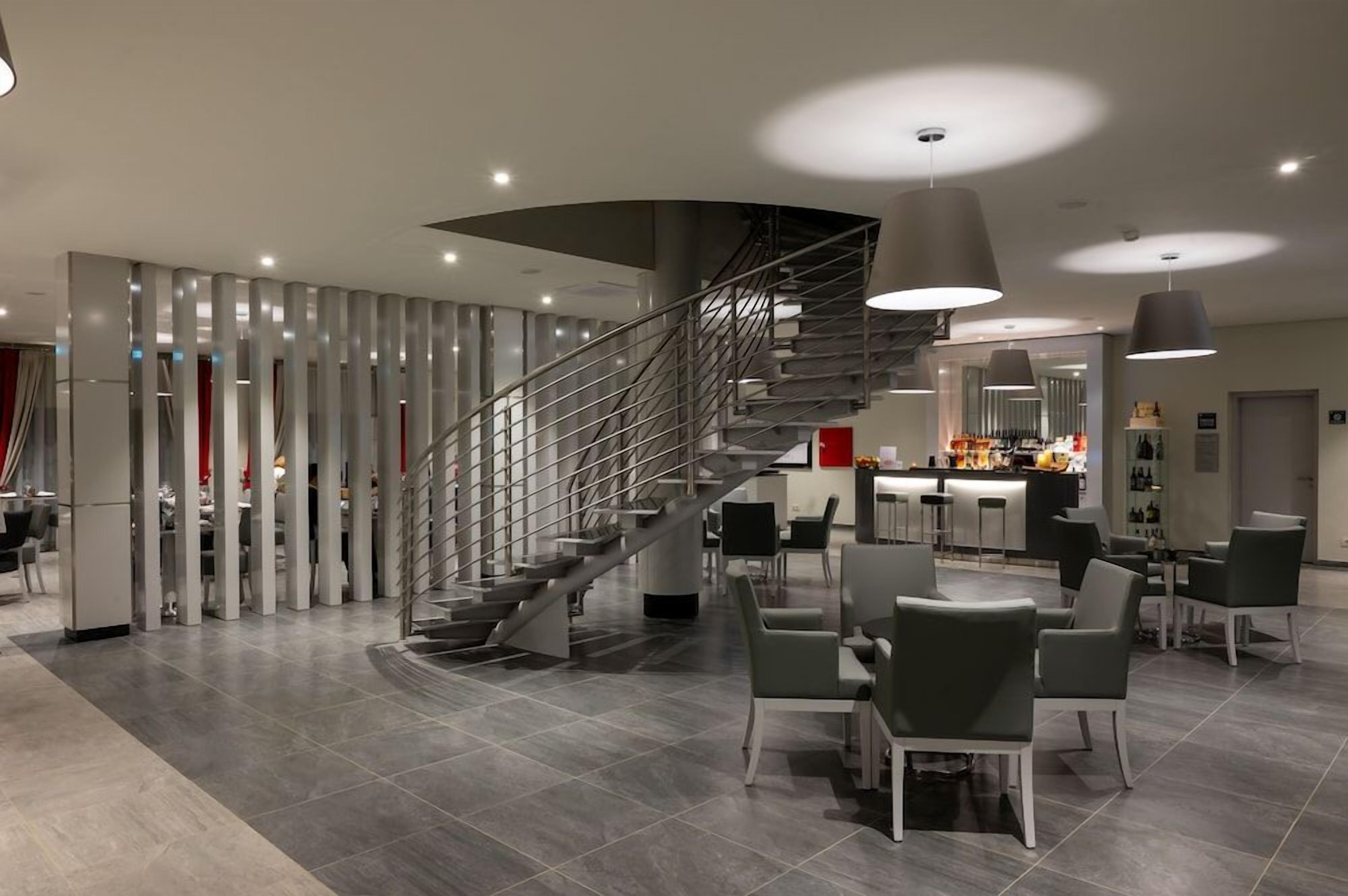Um interior moderno com uma escada curva, área de refeições com cadeiras e um bar.