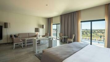 Habitación de hotel con cama, sofá, escritorio y balcón con vistas.