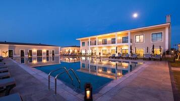 A hotel with a swimming pool, lounge chairs, and a well-lit exterior at dusk.