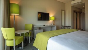 Et hotelværelse med en seng, et skrivebord, to stole, et fjernsyn og en lampe.
