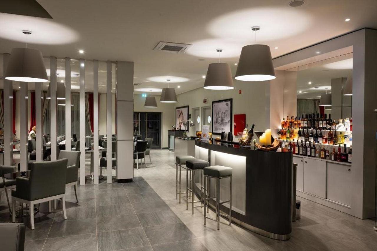 A modern bar area with high ceilings, pendant lighting, and a bar counter with a variety of bottles.