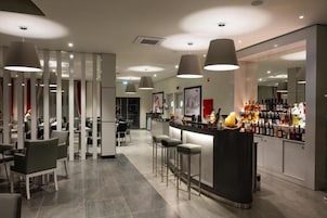 Zona de bar moderna con techos altos, iluminación colgante y una barra con una gran variedad de botellas.