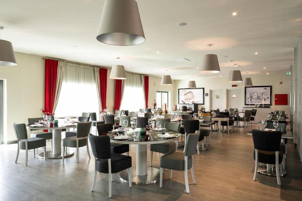 A spacious dining area with multiple tables and chairs, large pendant lights, and red curtains.
