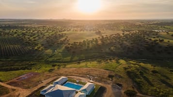 An aerial view of a property with a swimming pool, multiple buildings, and expansive green fields.