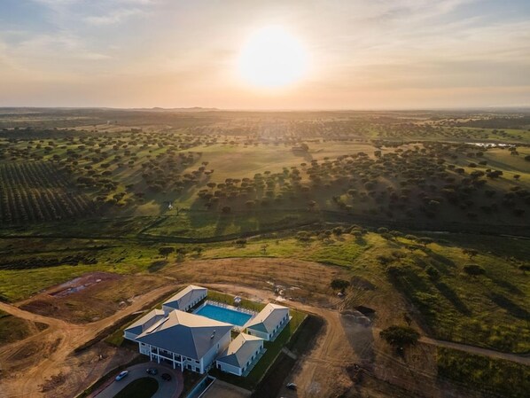 Vista aérea de una propiedad con piscina, varias edificaciones y amplios campos verdes.