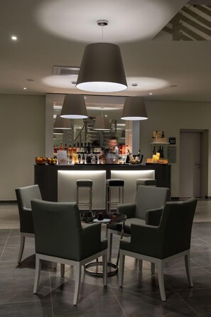 Zona de bar con mostrador, taburetes y luces colgantes.