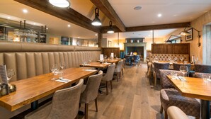 Ein Restaurantinnenraum mit Holztischen, gepolsterten Sitzecken und Pendelleuchten.