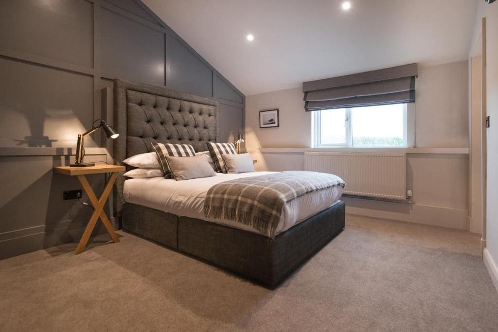 A bedroom with a large bed, bedside tables, a window with blinds, and a radiator.