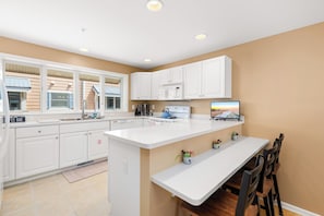 A modern kitchen with white cabinetry, a built-in microwave, and a large island with a sink. - Oceanside,Pool,Skee-ball,Nintendo,Pets,Arcades (Ocean City)