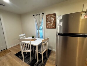Una cocina con un refrigerador de acero inoxidable, una mesa de comedor con sillas, una planta en maceta y un letrero en la pared.