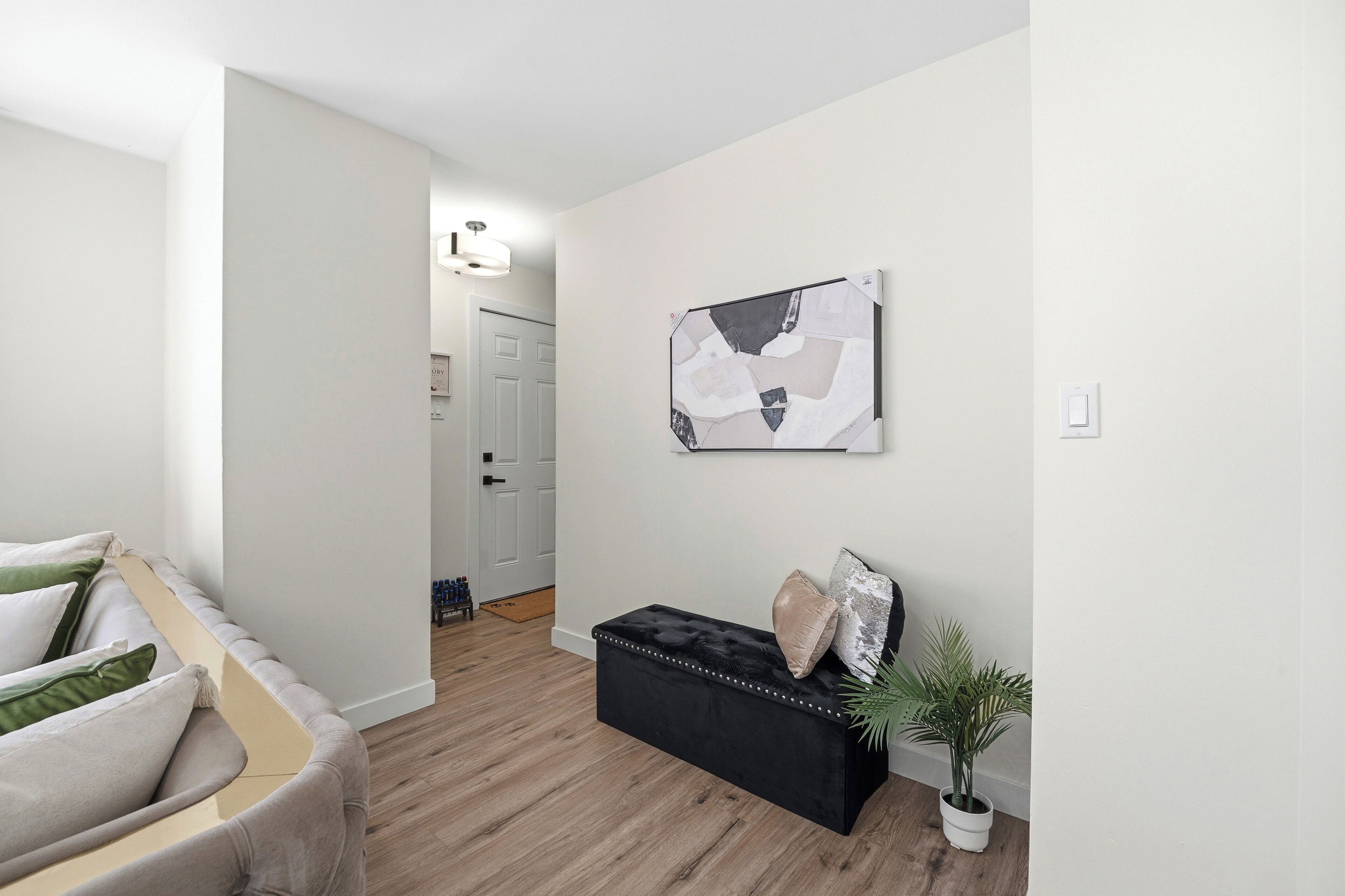A modern living room with a sofa, a black ottoman, and a wall-mounted abstract painting.