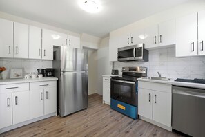 A modern kitchen with white cabinets, stainless steel appliances, and a wooden floor.