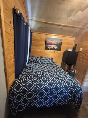 A wooden-paneled room with a bed, a painting on the wall, and a heater.