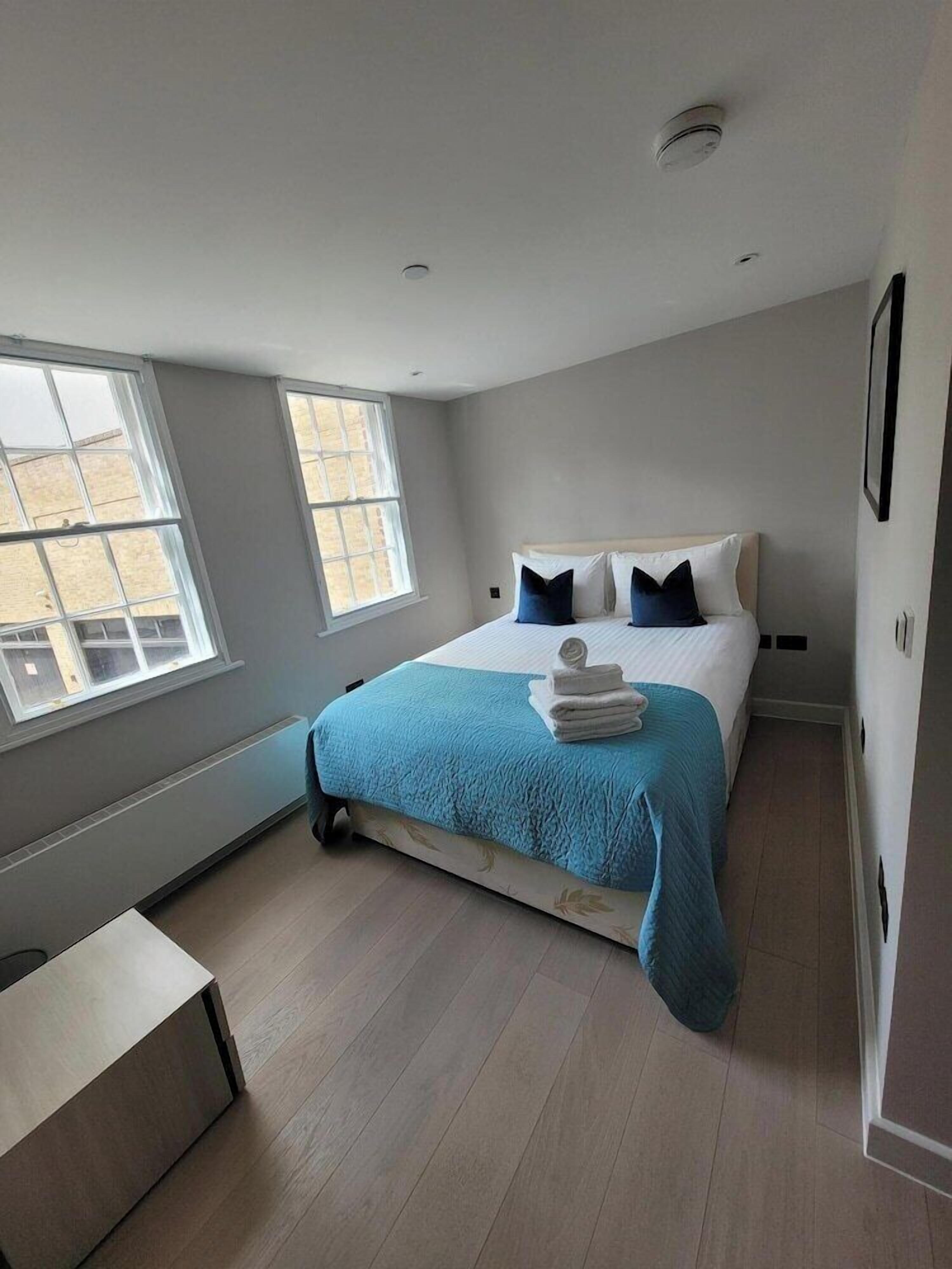 A bedroom with a bed, two windows, a bedside table, and a chair.
