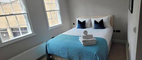 A bedroom with a bed, two windows, a bedside table, and a chair.