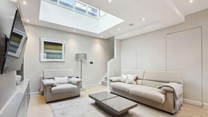 A modern living room with a flat-screen TV, two sofas, a coffee table, and a skylight. - Buckingham Palace Residences by Aeria Apartments (London)