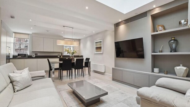 A modern living room with a sofa, coffee table, and a dining area with chairs and a table. - Buckingham Palace Residences by Aeria Apartments (London)