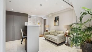 A modern living room with a sofa, a dining area with a table and chairs, and a kitchen area with cabinets. - Buckingham Palace Residences by Aeria Apartments (London)