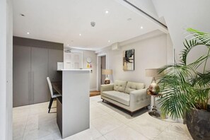 A modern living room with a sofa, a dining area with a table and chairs, and a kitchen area with cabinets.