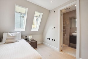 A bedroom with a bed, bedside table, lamp, and two windows.